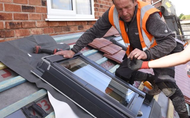 A roofer in a high vis jacket installing roof window flashing